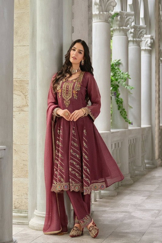 Woman in a maroon traditional outfit with embroidery, standing in an elegant interior setting.